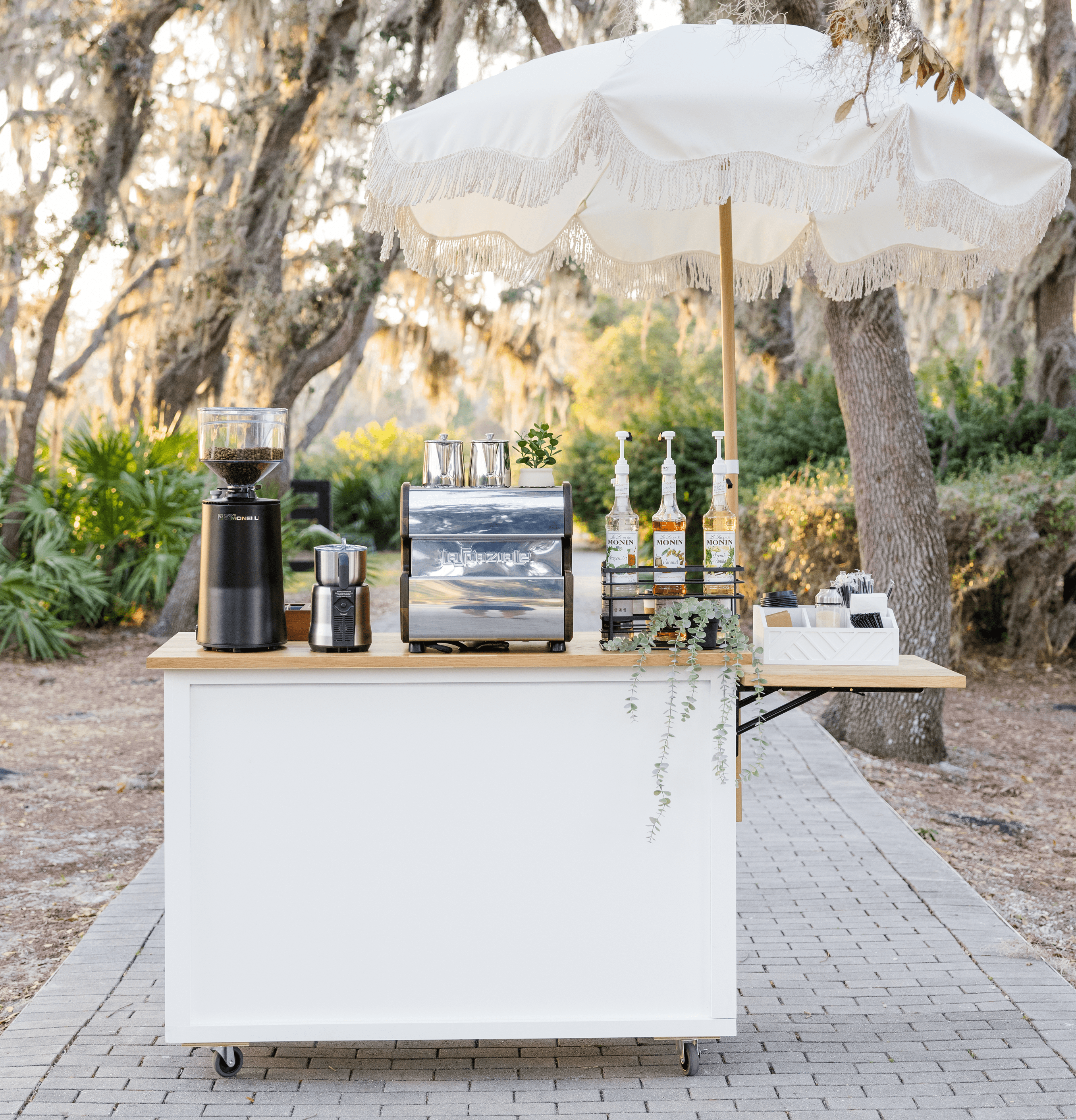 Elegant mobile coffee cart setup with espresso machine, grinder, and syrup dispensers under a decorative umbrella